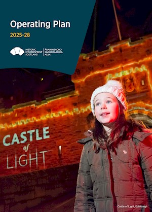A girl in a woolly hat and padded coat standing in front of the entrance to Edinburgh Castle which is lit in red and has the words 'Castle of Light' projected onto it
