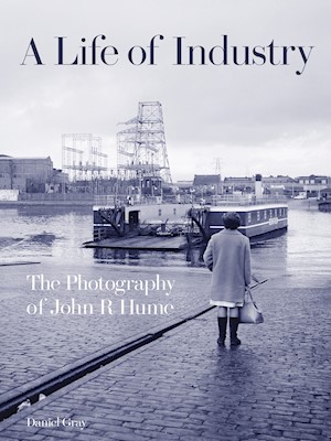 A person standing on a slipway watching a boat as it sails down the river